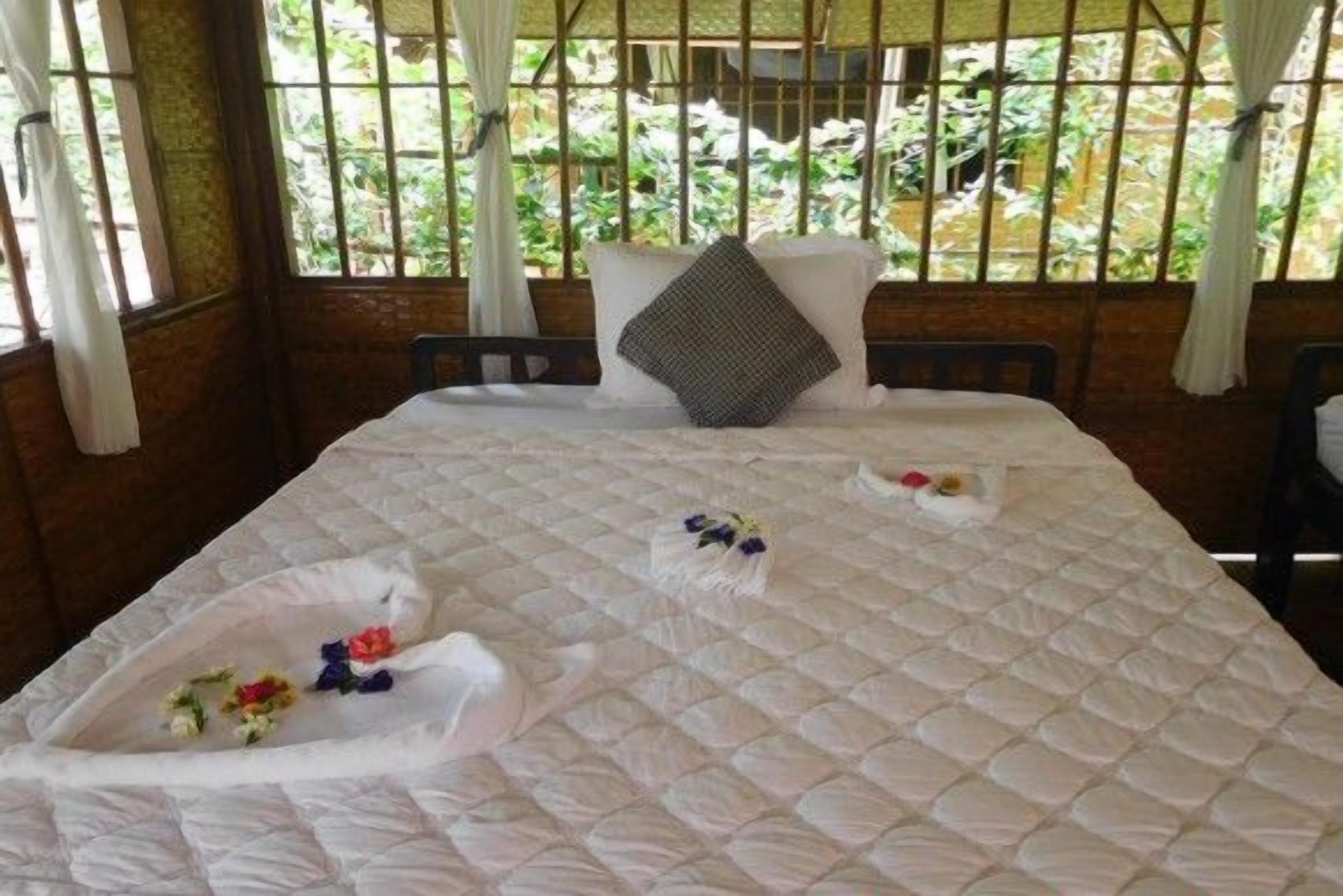 A bed with a quilted white bedspread, two pillows, and a decorative arrangement of flowers on the bed.