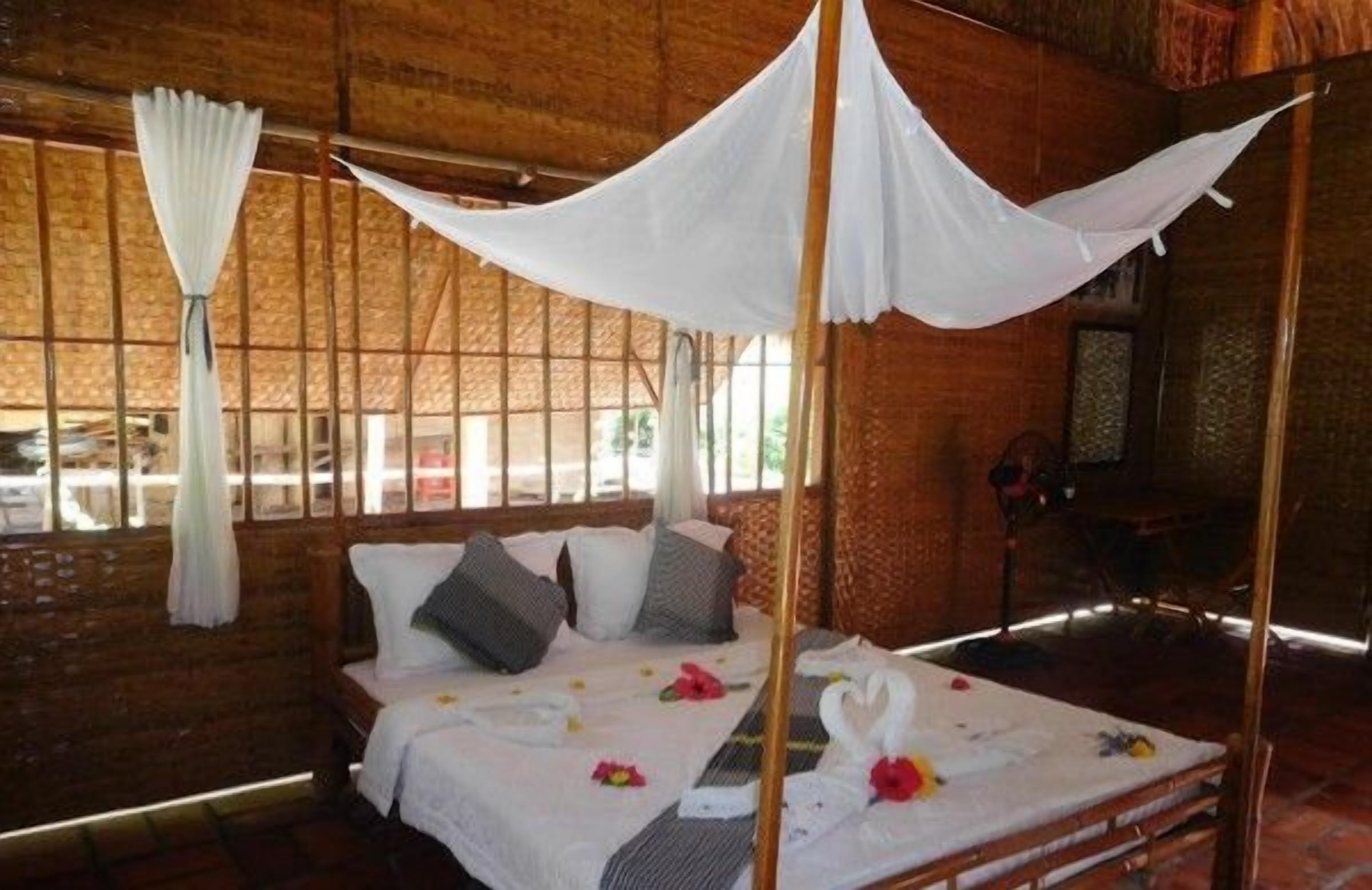 Un letto a baldacchino, cuscini e decorazioni floreali in una stanza con pareti in legno e finestre.