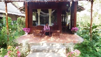 A covered outdoor seating area with wooden furniture and a thatched roof.