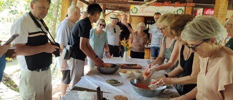 A group of people preparing food outdoors at a table with various ingredients and utensils.
