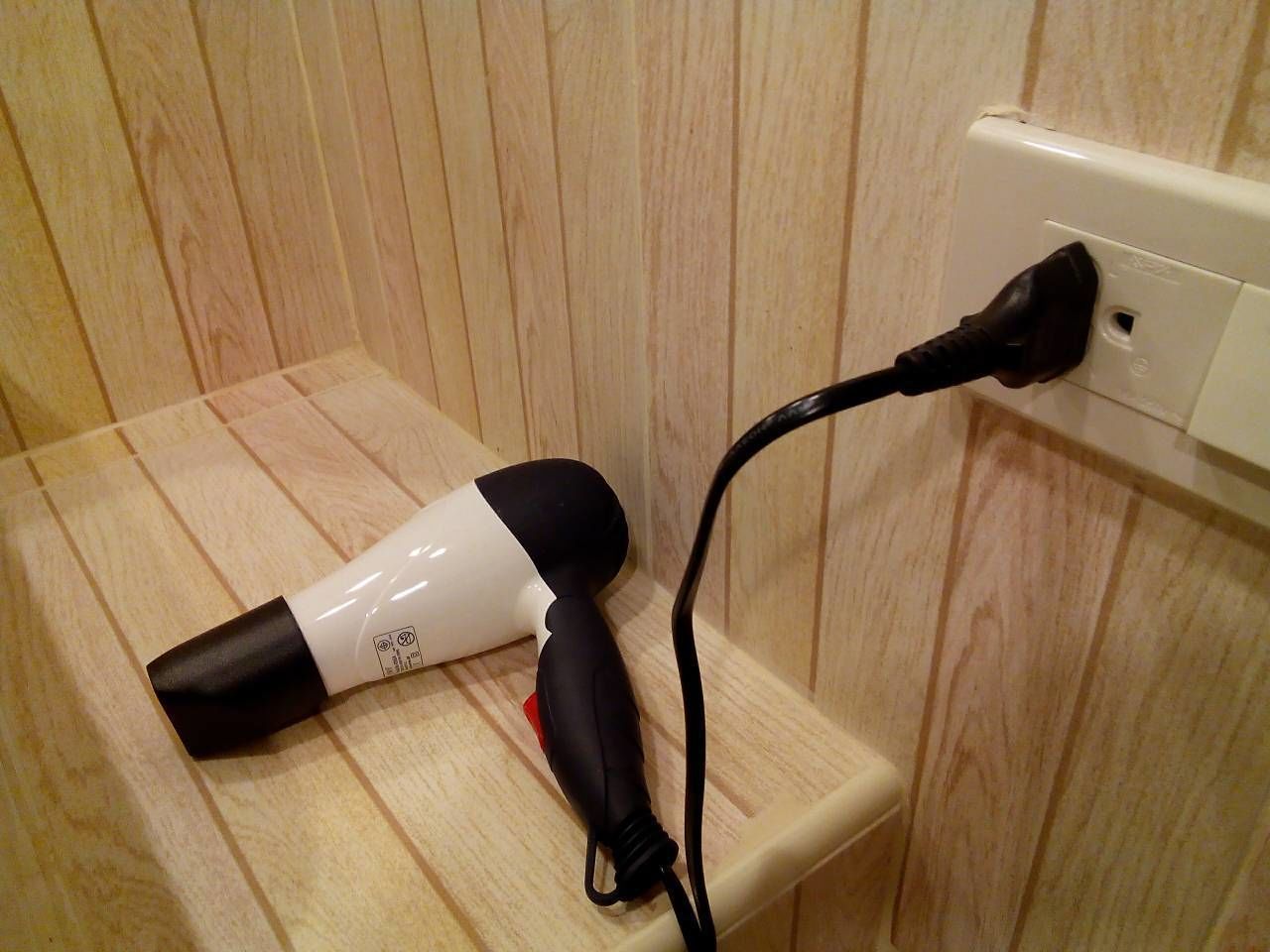 A hair dryer plugged into a wall socket in a room with wooden paneling.