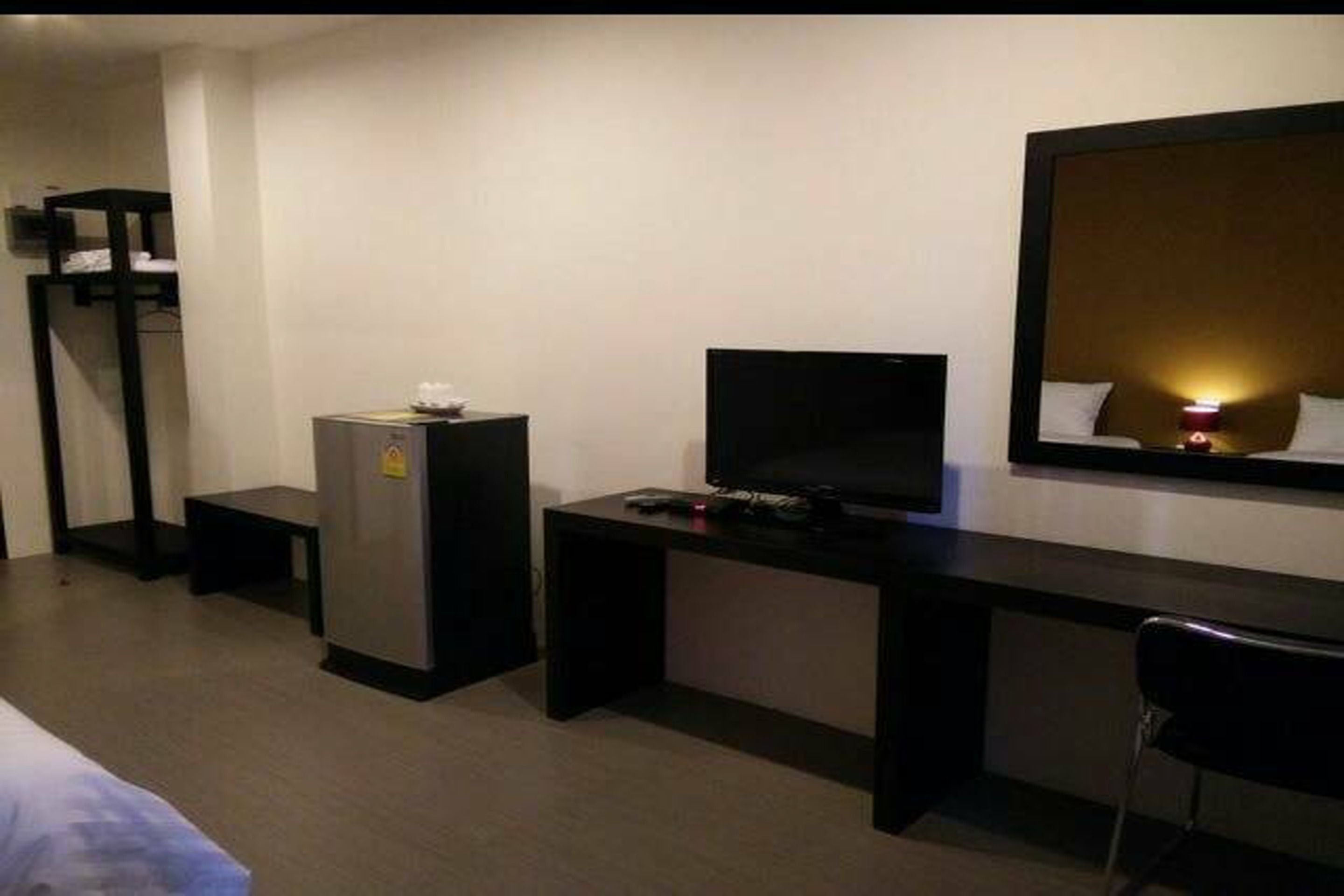 A hotel room with a bed, a desk with a computer, a small refrigerator, and a mirror.