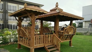A wooden gazebo with a roof and steps, surrounded by a well-maintained lawn. - One Fu Hotel (Surin)