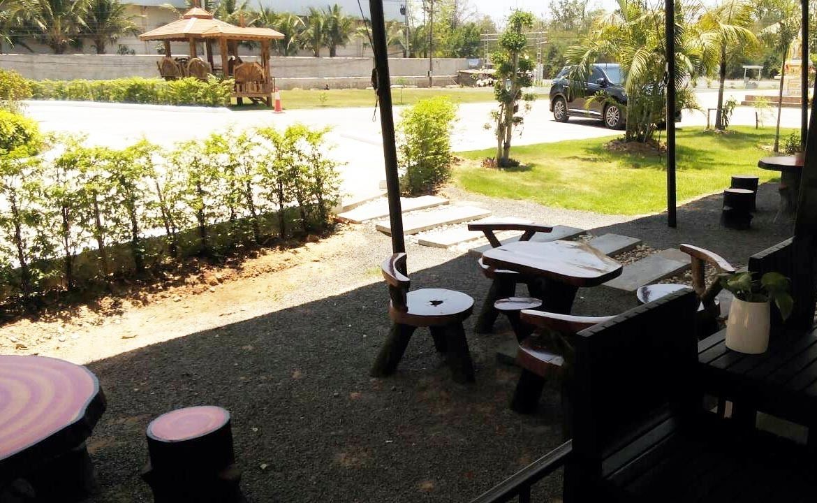 An outdoor seating area with tables and chairs, a gazebo, and a view of a road and greenery.