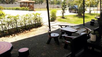 An outdoor seating area with tables and chairs, a gazebo, and a view of a road and greenery.