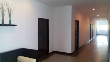 Un pasillo largo y estrecho con un banco a la izquierda, puertas a la derecha y un ventanal grande al final.