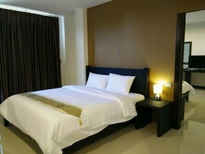 A hotel room with a large bed, a bedside table with a lamp, a mirror, and a window with curtains.