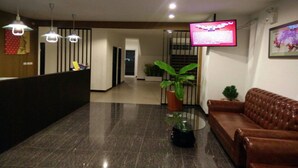 A reception area with a reception desk, a brown leather sofa, a potted plant, and a television screen. - One Fu Hotel (Surin)