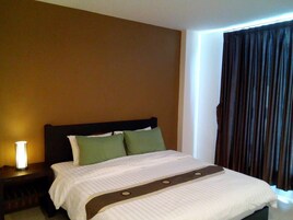 Una habitación de hotel con una cama, una mesita de noche con lámpara y una ventana con cortinas.