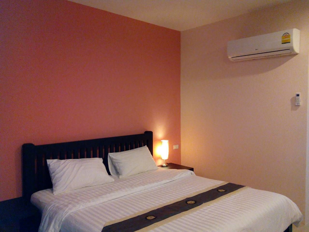 Una habitación de hotel con una cama, una mesita de noche, aire acondicionado de pared y una lámpara de pared.