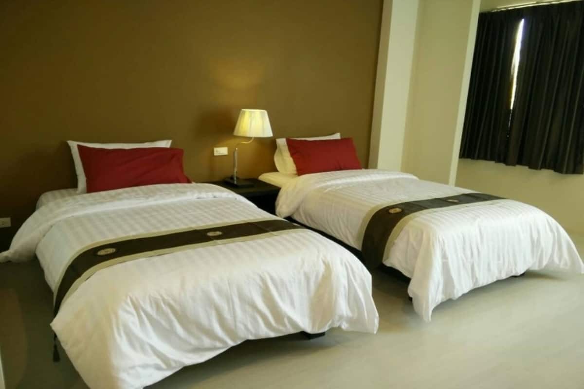 Habitación de hotel con dos camas, cada una con ropa blanca y almohadas rojas. Entre las camas, una mesita de noche con lámpara.