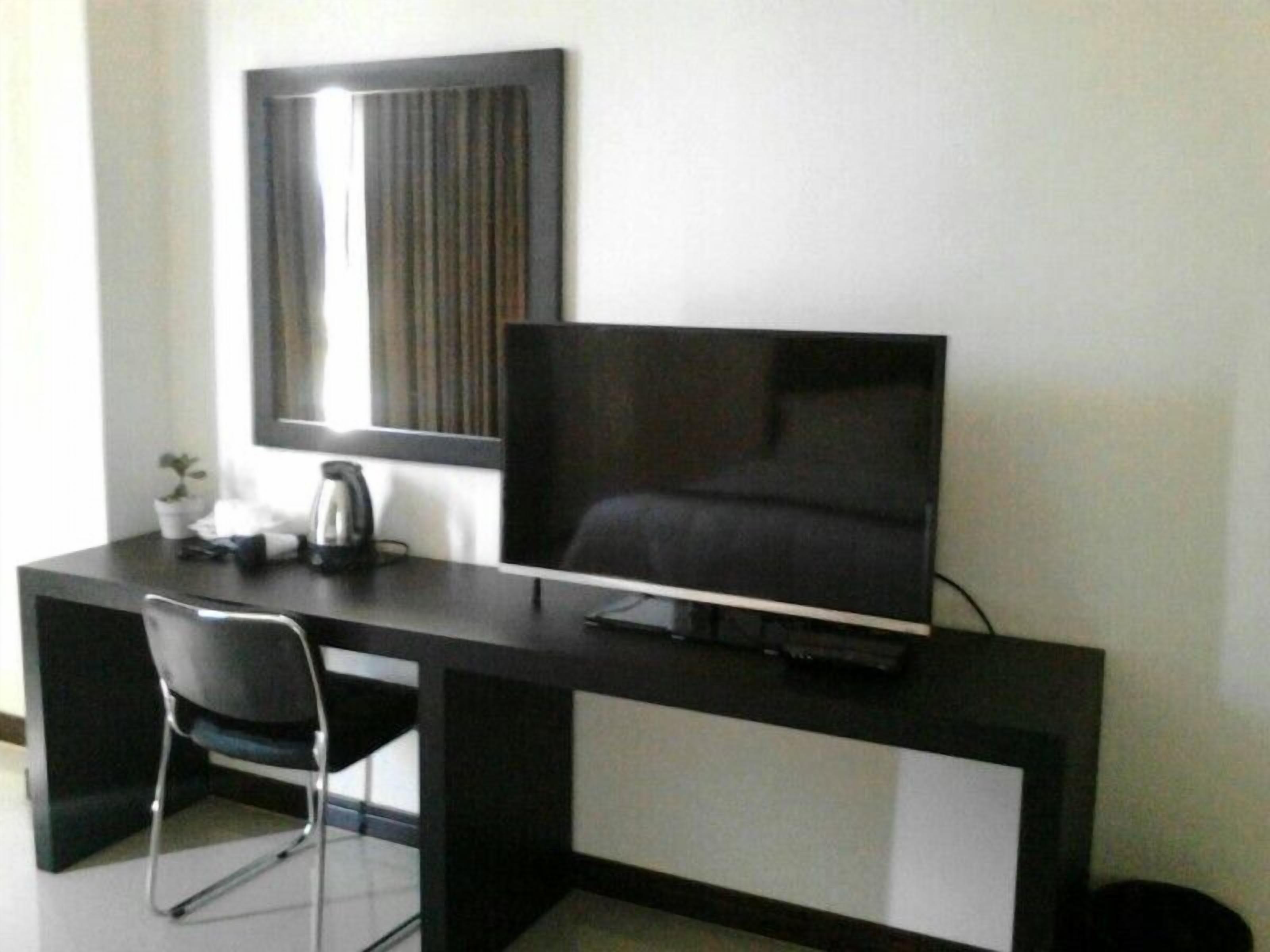 A modern hotel room with a dark-colored desk, a flat-screen TV, a chair, and a small potted plant.