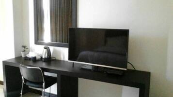 A modern hotel room with a dark-colored desk, a flat-screen TV, a chair, and a small potted plant.