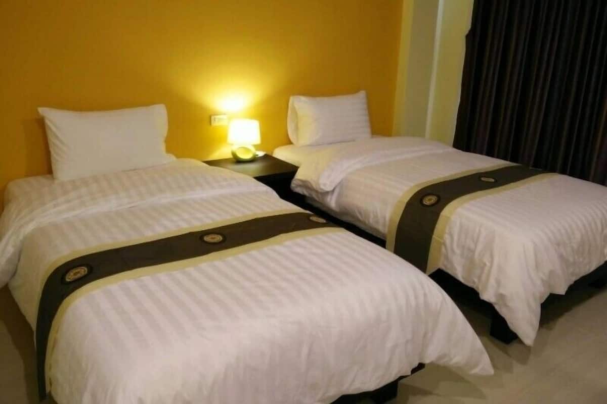 Habitación de hotel con dos camas, cada una con ropa blanca y detalles oscuros. Entre las camas, una mesita de noche con una lámpara.