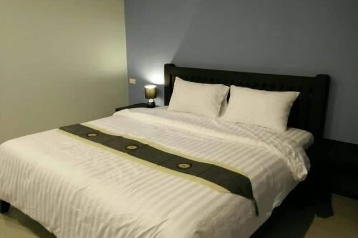 Una cama bien hecha con una colcha blanca y verde, un cabecero oscuro y una mesita de noche con una lámpara.