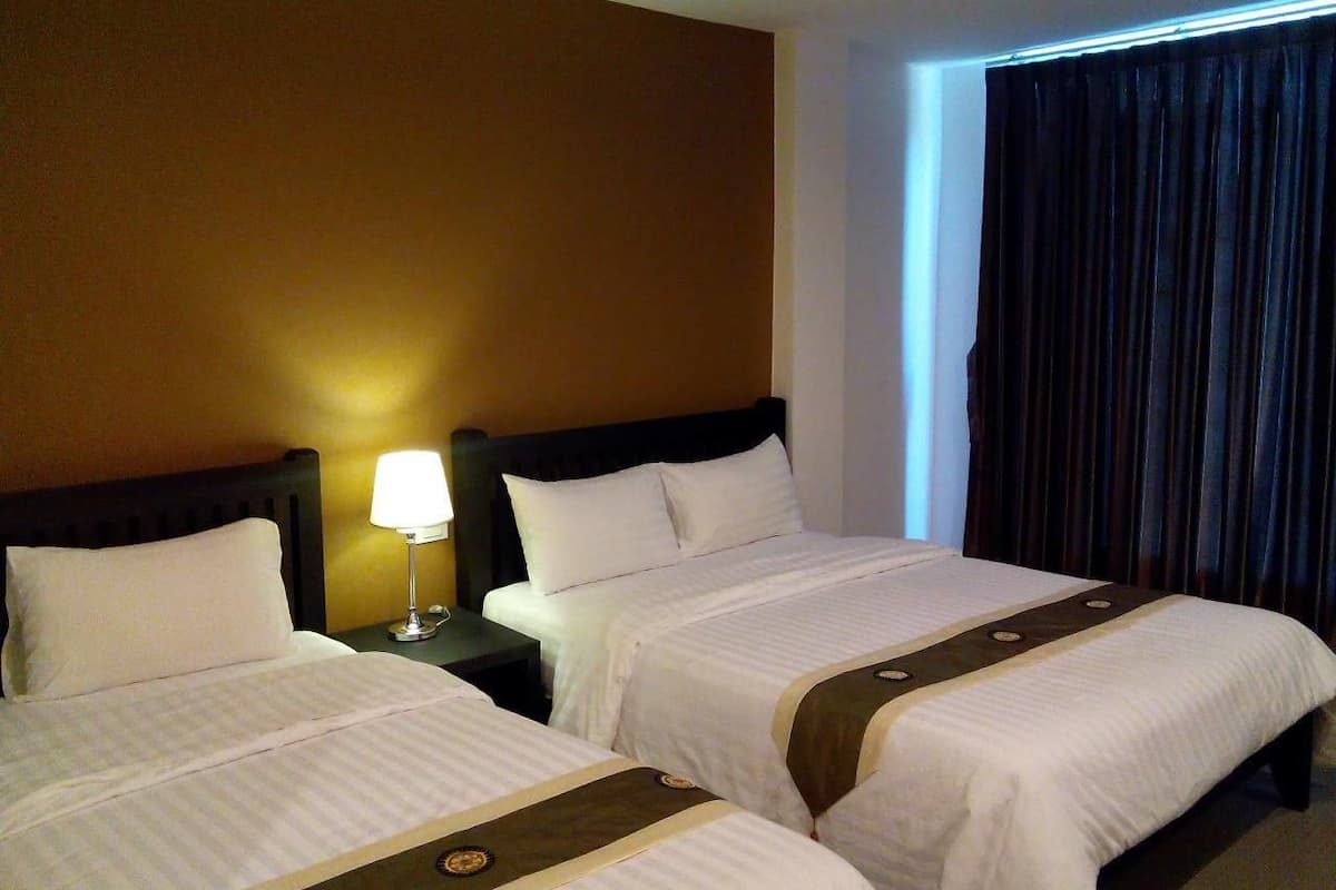 Una habitación de hotel con dos camas, una mesita de noche con lámpara y una ventana con cortinas.