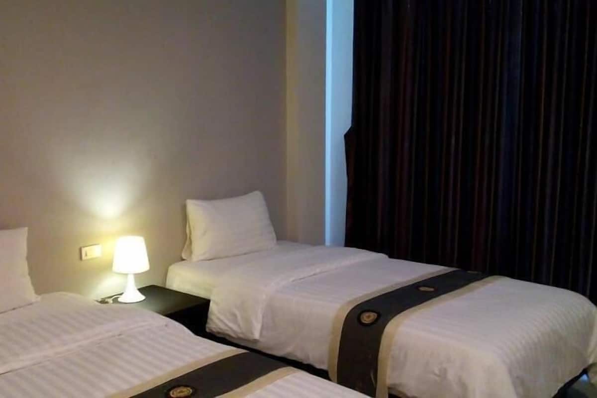 Una habitación de hotel con dos camas, una mesita de noche con lámpara y una cortina oscura.