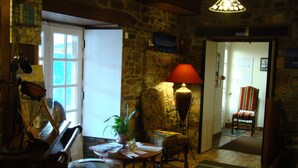 A cozy room with a stone wall, a wooden table, a chair, a lamp, and a television on the wall. - Hotel du Tertre (Mont-Dol)