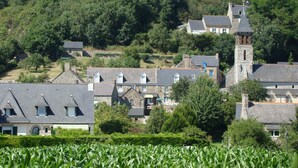 A rural village with traditional stone buildings, a prominent church tower, and a cross on a hill. - Hotel du Tertre (Mont-Dol)