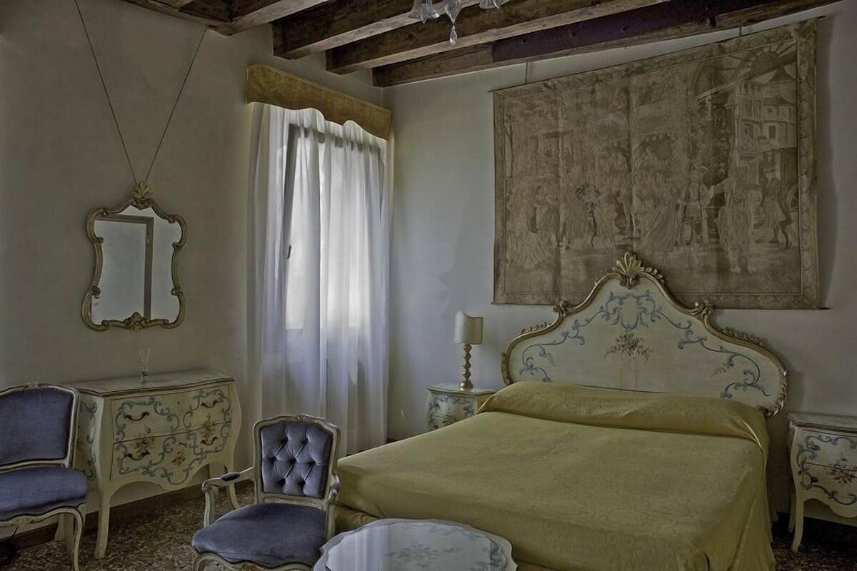 Ein Zimmer mit einem Bett, einem Sessel, einem Schminktisch und einem Spiegel.