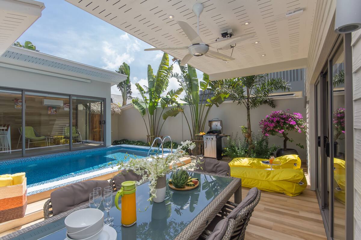 Une terrasse extérieure moderne avec une table en verre, un pouf jaune et une piscine.
