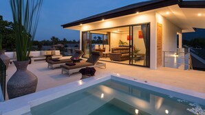 A modern outdoor living area with a pool, lounge chairs, and a glass-enclosed dining area. -  Ban Tai Estate Villas (Koh Samui)