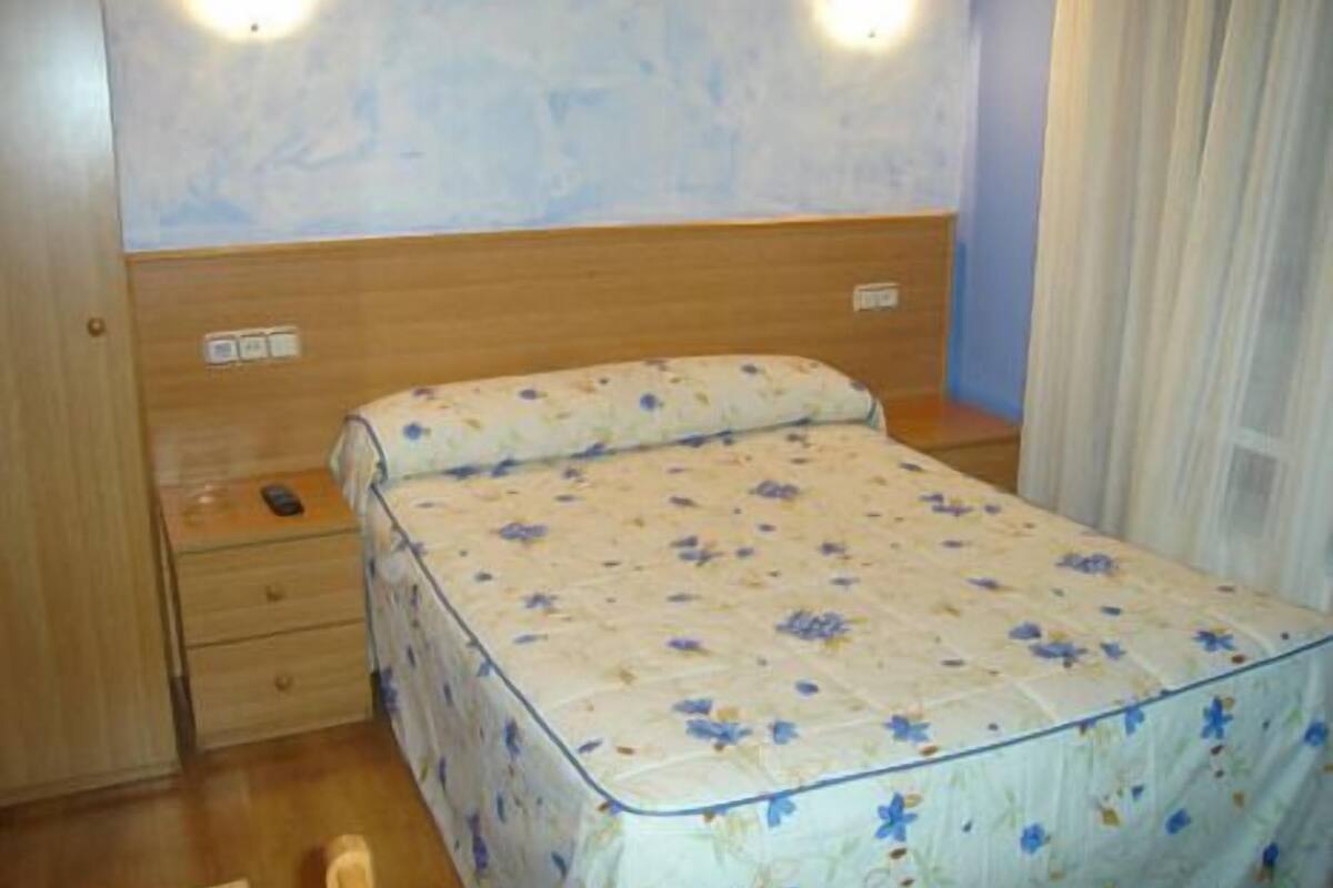 Un dormitorio con cabecera de madera, una cama individual con colcha floral, una mesita de noche y un aplique de pared.