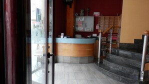 A reception area with a counter, a bulletin board, and a staircase leading to an upper floor. - Hotel Doña María (Gijon)