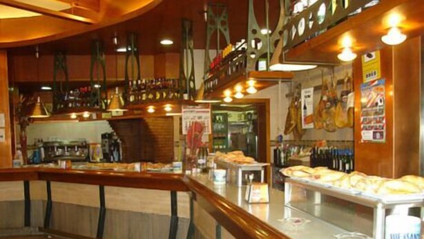 A bar area with a counter displaying pastries and bottles. - Hotel Doña María (Gijon)