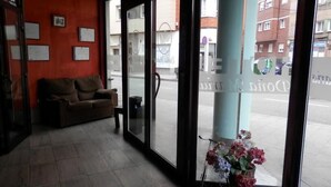 A lobby with a brown sofa, a trash bin, and a vase with flowers. - Hotel Doña María (Gijon)