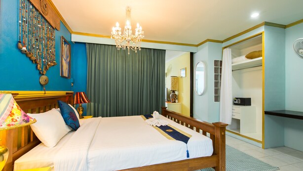 Una cama bien hecha con cabecera de madera, un candelabro, un reloj de pared y un espejo.