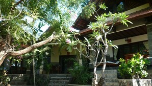 Un patio con una escalera de piedra que conduce a un edificio, rodeado de abundante vegetación y un árbol con flores rosadas.