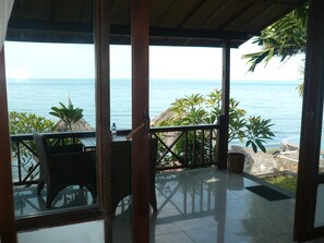 A covered outdoor area with a view of the sea, featuring wicker furniture and a thatched-roof structure. - Wawa Wewe II Villas (Karangasem)