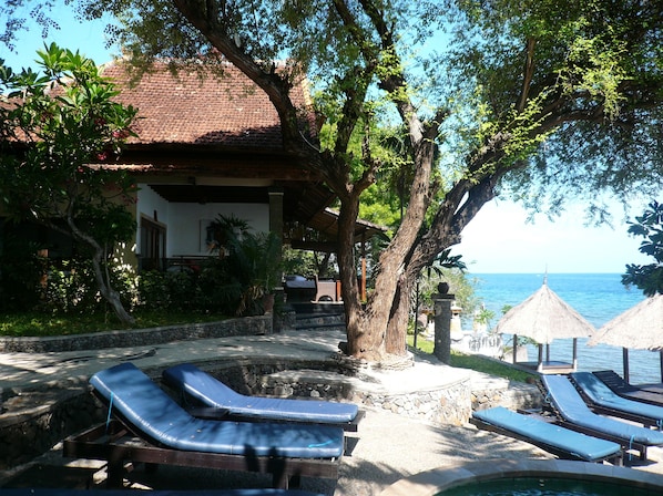 A poolside area with lounge chairs, a stone wall, and a view of the sea.