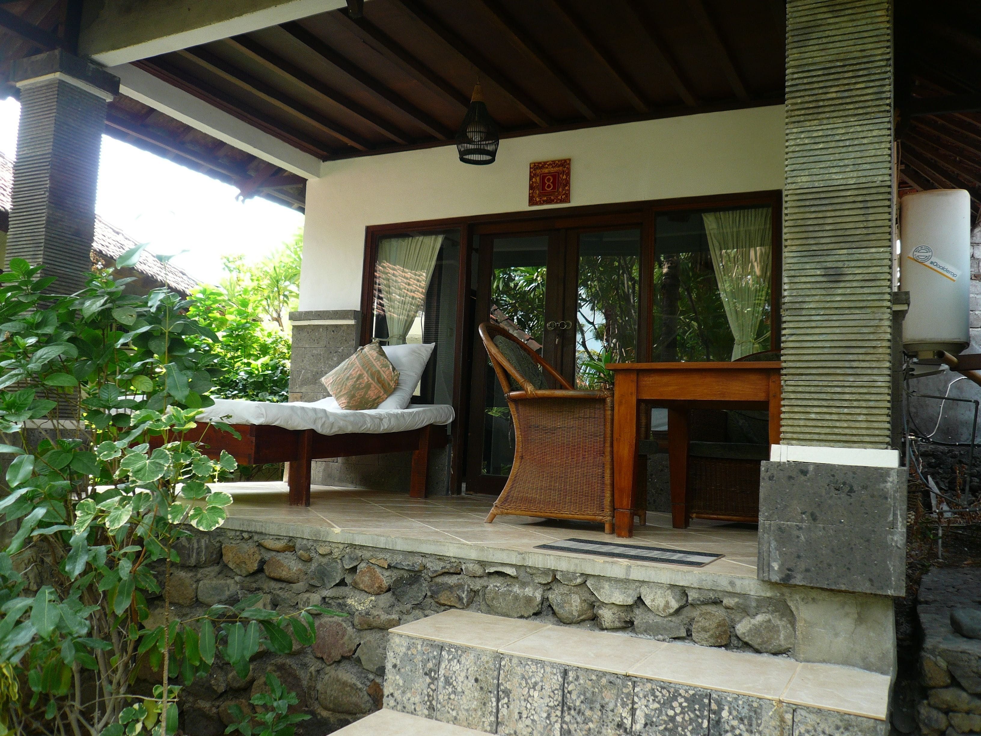 A covered outdoor seating area with a cushioned bench, a wicker chair, and a table.