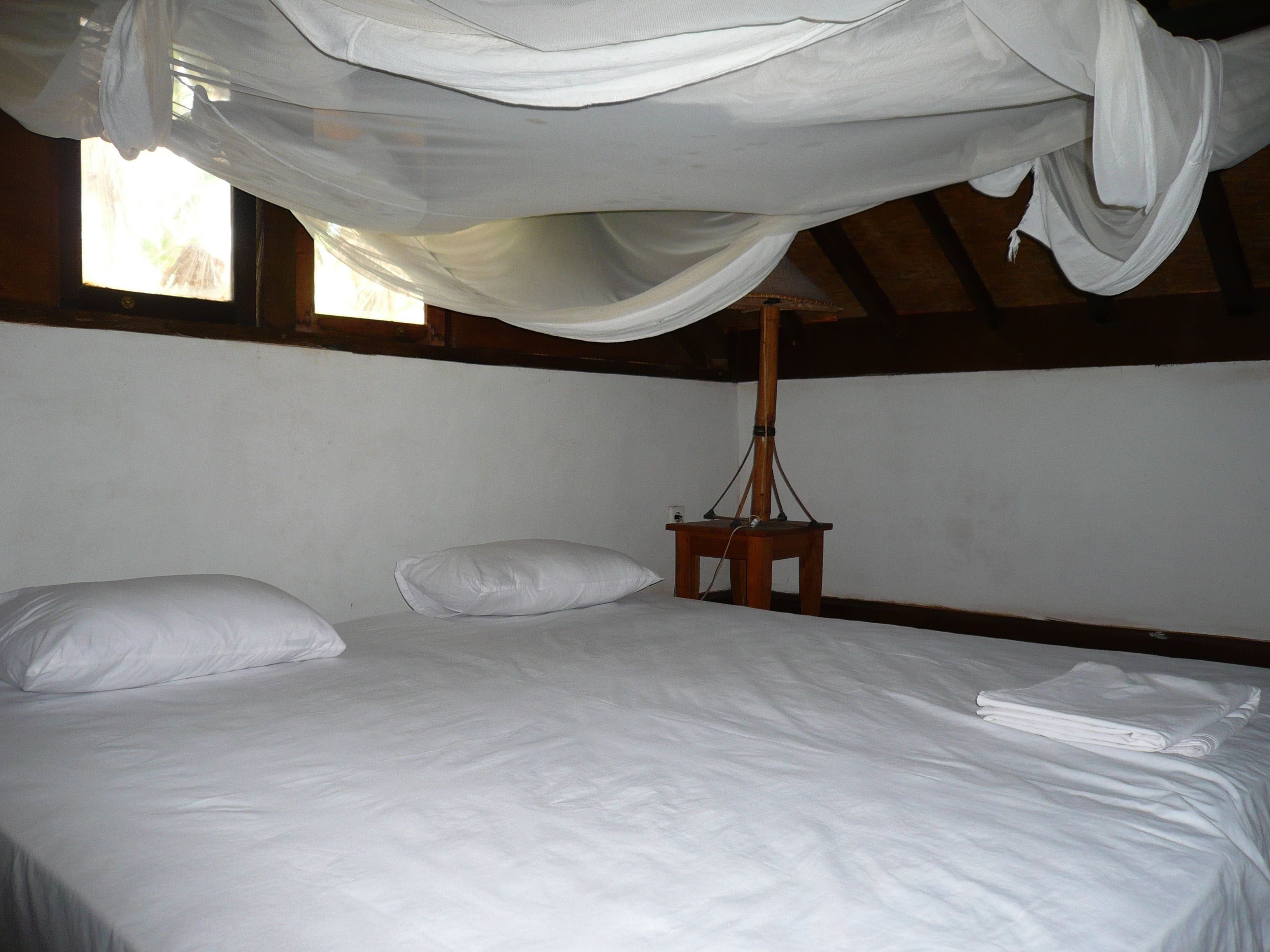 Una cama con sábanas blancas, una mesita de noche de madera y un dosel colgante.