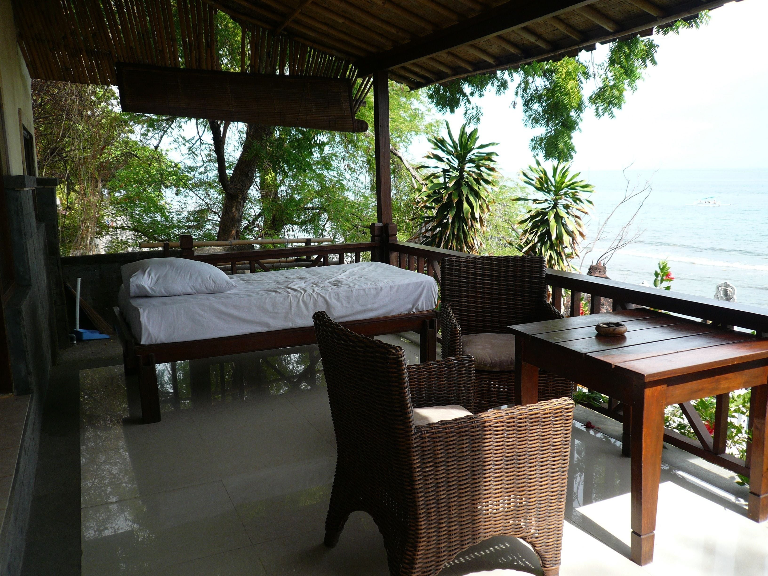 Una habitación con una cama, sillas de mimbre, una mesa y vista al mar.