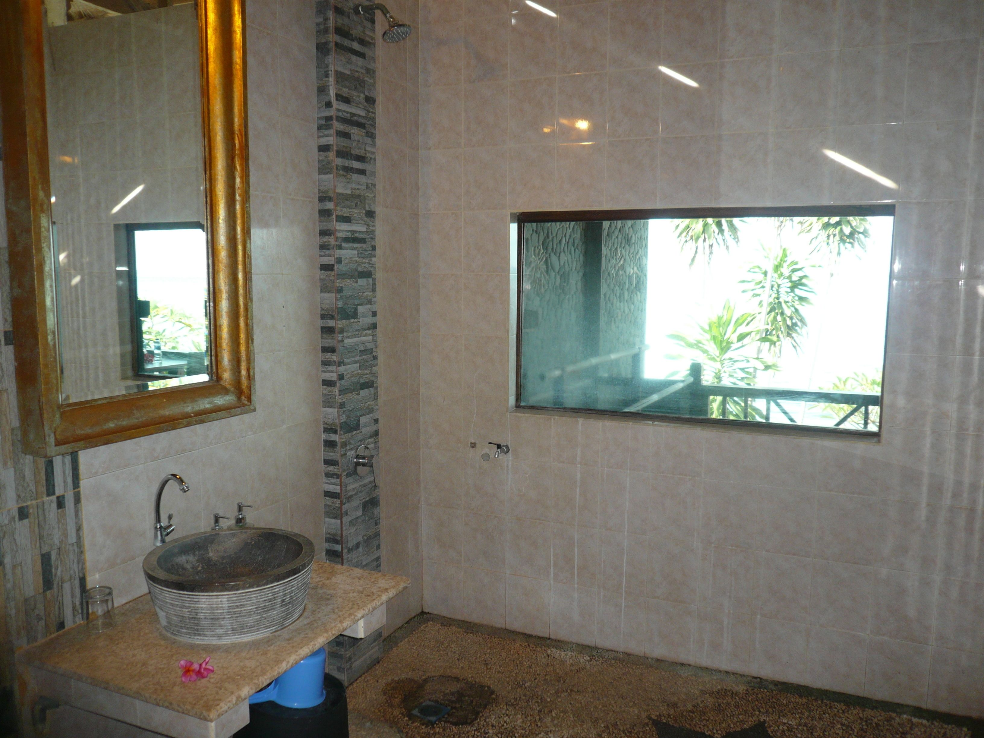A bathroom with a stone sink, a large mirror, and a window with a view of greenery.