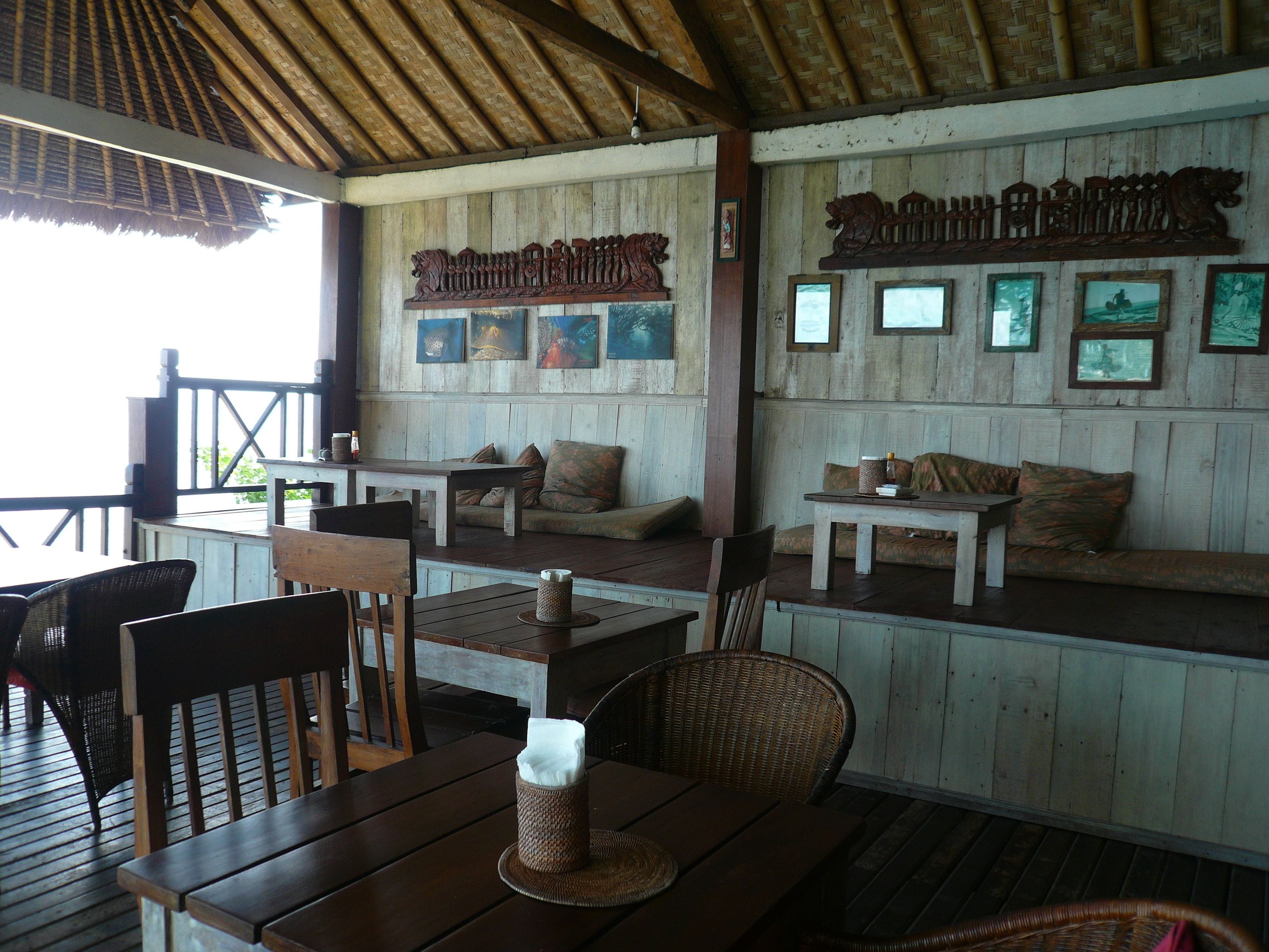 A wooden deck with tables and chairs, a wooden wall with framed pictures, and a sign above the seating area.