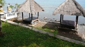 Dos construcciones con techo de paja, bancos, un sendero de piedra y vista al mar.