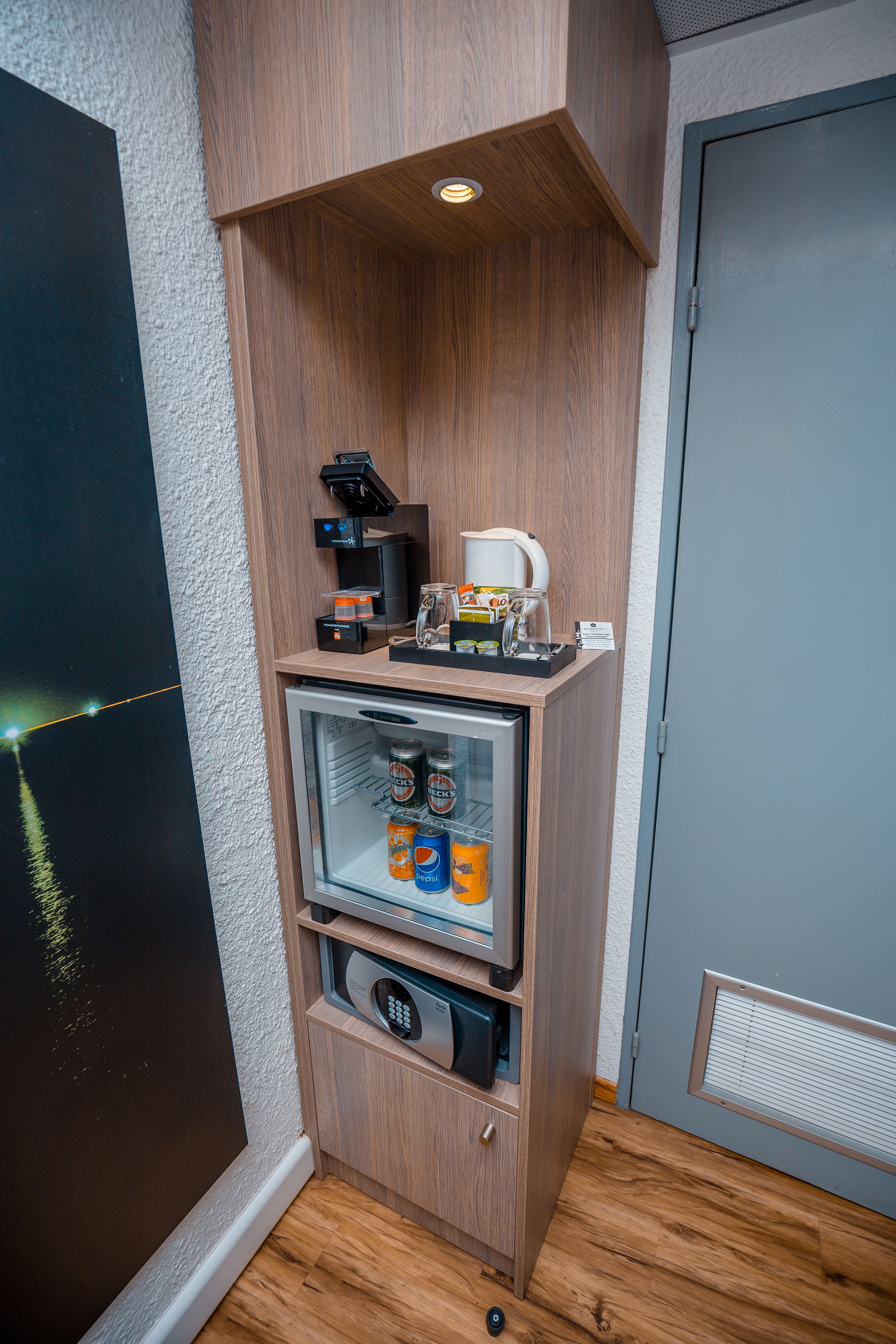 A compact minibar with a coffee machine, a glass of water, and a coffee pot.