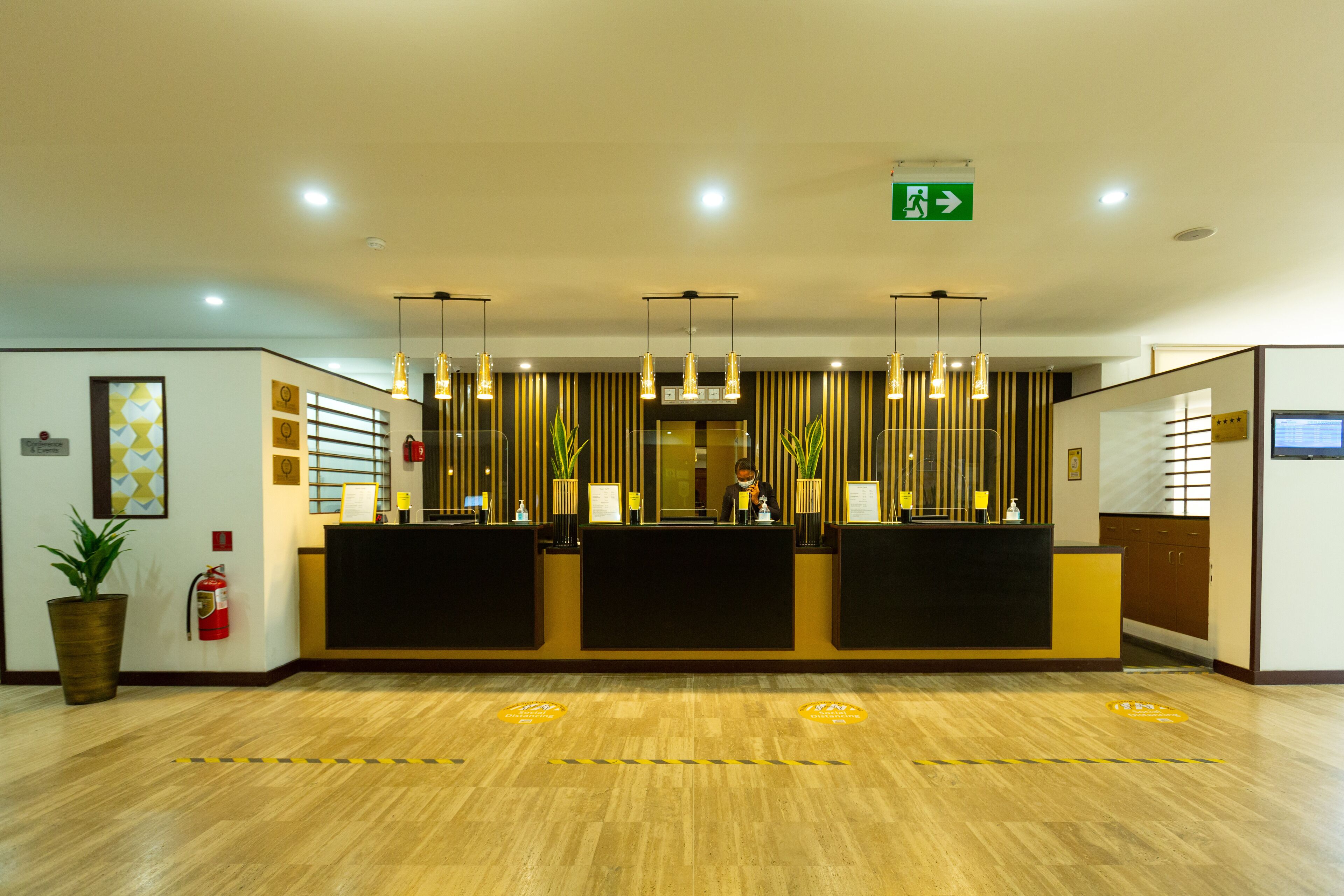 Zona de recepción de un hotel con un mostrador, un extintor y una planta en maceta.
