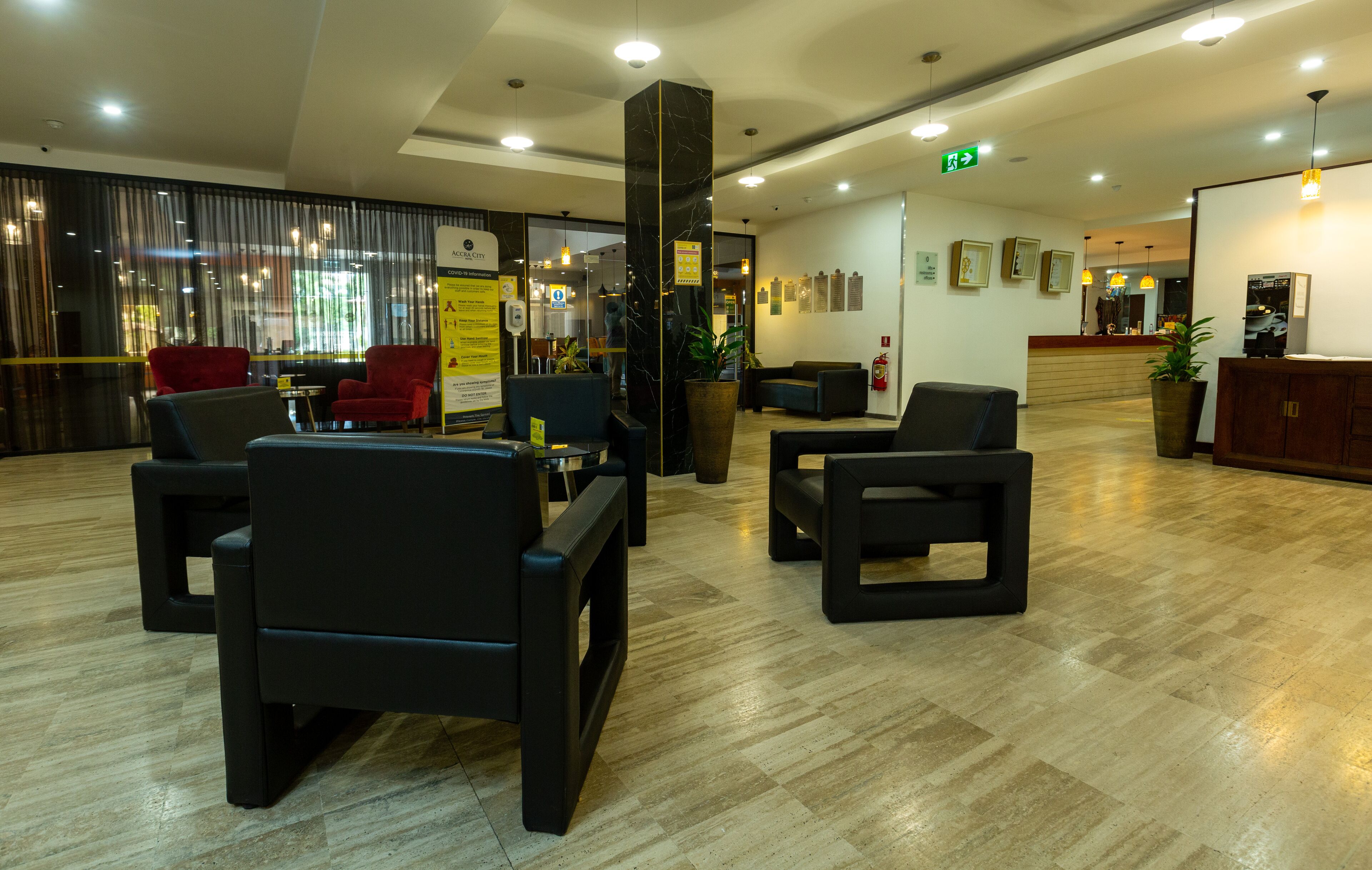 A modern lobby with black leather seating, a large marble pillar, and a wooden reception desk.