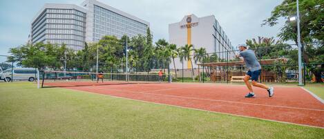 A tennis court with a net, surrounded by greenery and buildings.