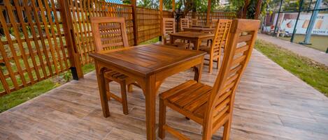 Un patio exterior de madera con mesas y sillas, rodeado por una valla de madera y follaje.