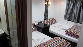 Habitación de hotel con dos camas individuales, una mesita, un teléfono y una ventana con cortinas.