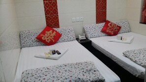 Two single beds with floral-patterned bedspreads and matching pillows, a nightstand with a telephone and toiletries, and a decorative accent wall.