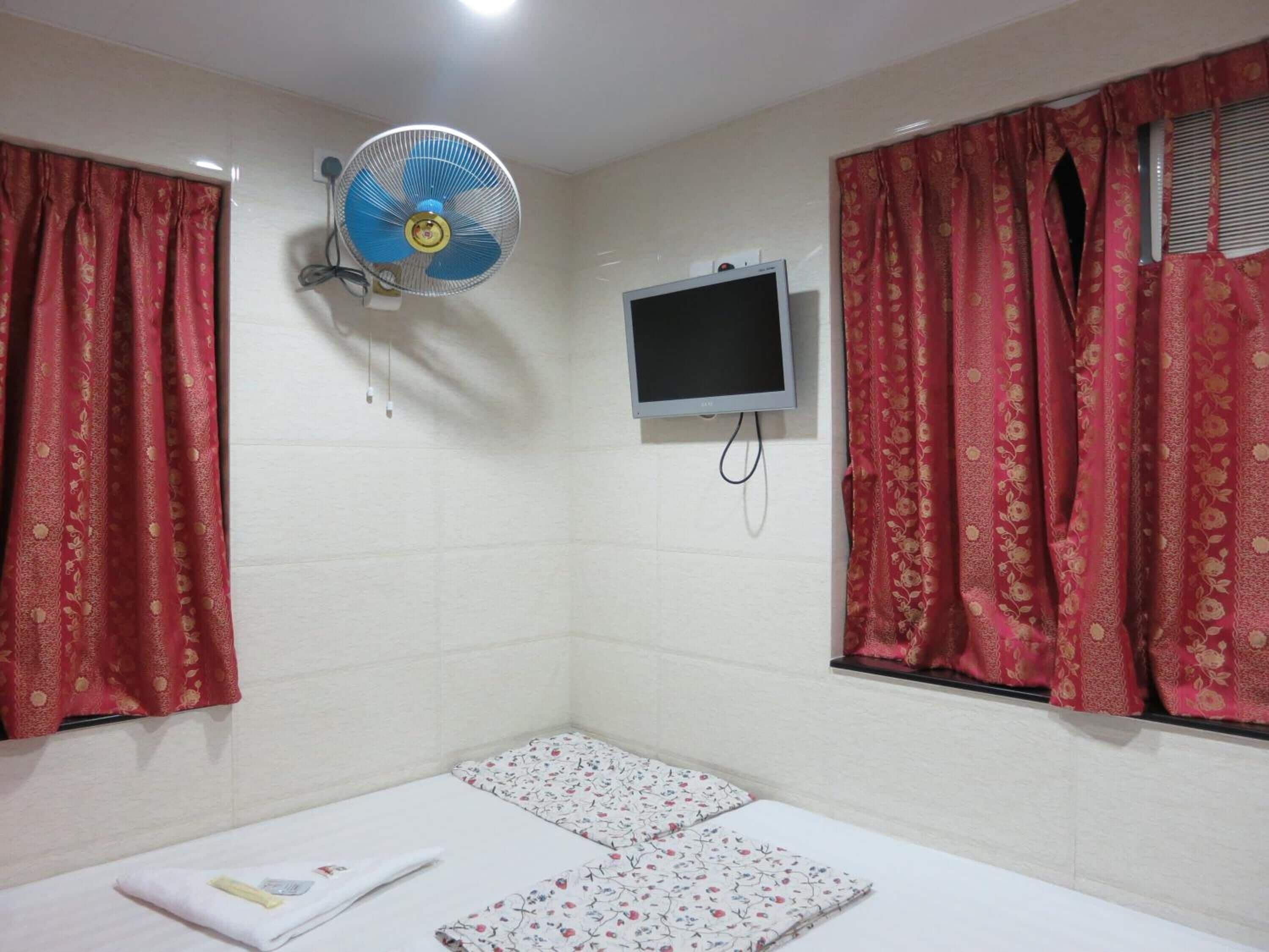 A small room with a bed, a wall-mounted TV, and a ceiling fan.