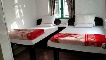 Two single beds with white linens and red blankets, a window with curtains, and a tiled floor.
