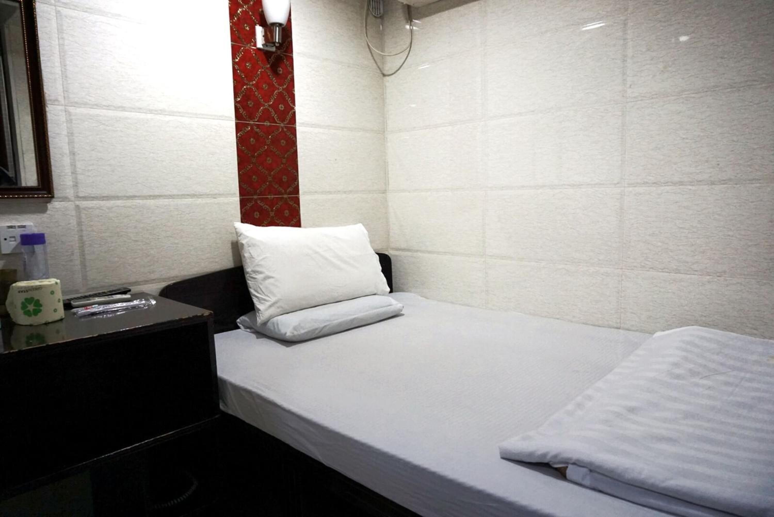 Quarto de hotel pequeno e limpo, com uma cama de solteiro, mesa de cabeceira e um espelho.